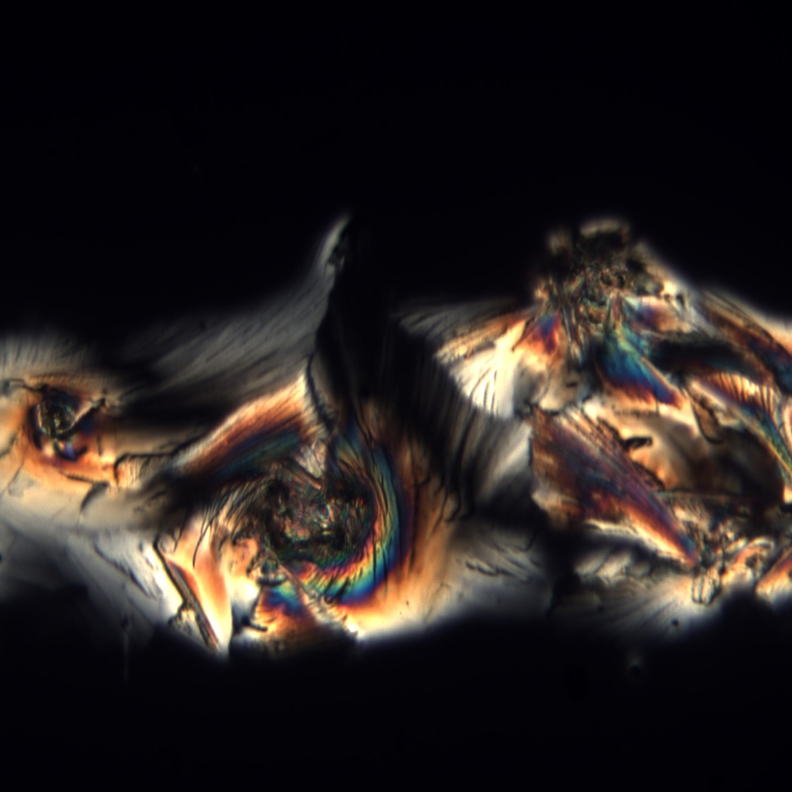 Radiating crystal formation in warm amber and teal, cross-polarized light detail