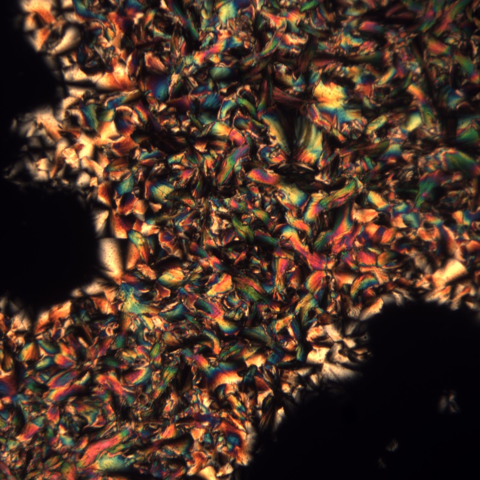Dense mosaic of crystal facets in amber, green, and blue, cross-polarized light detail